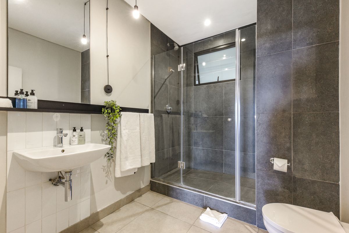 Modern bathroom featuring a glass-enclosed shower, wall-mounted basin with chrome fixtures, and contemporary dark and light tile finishes.
