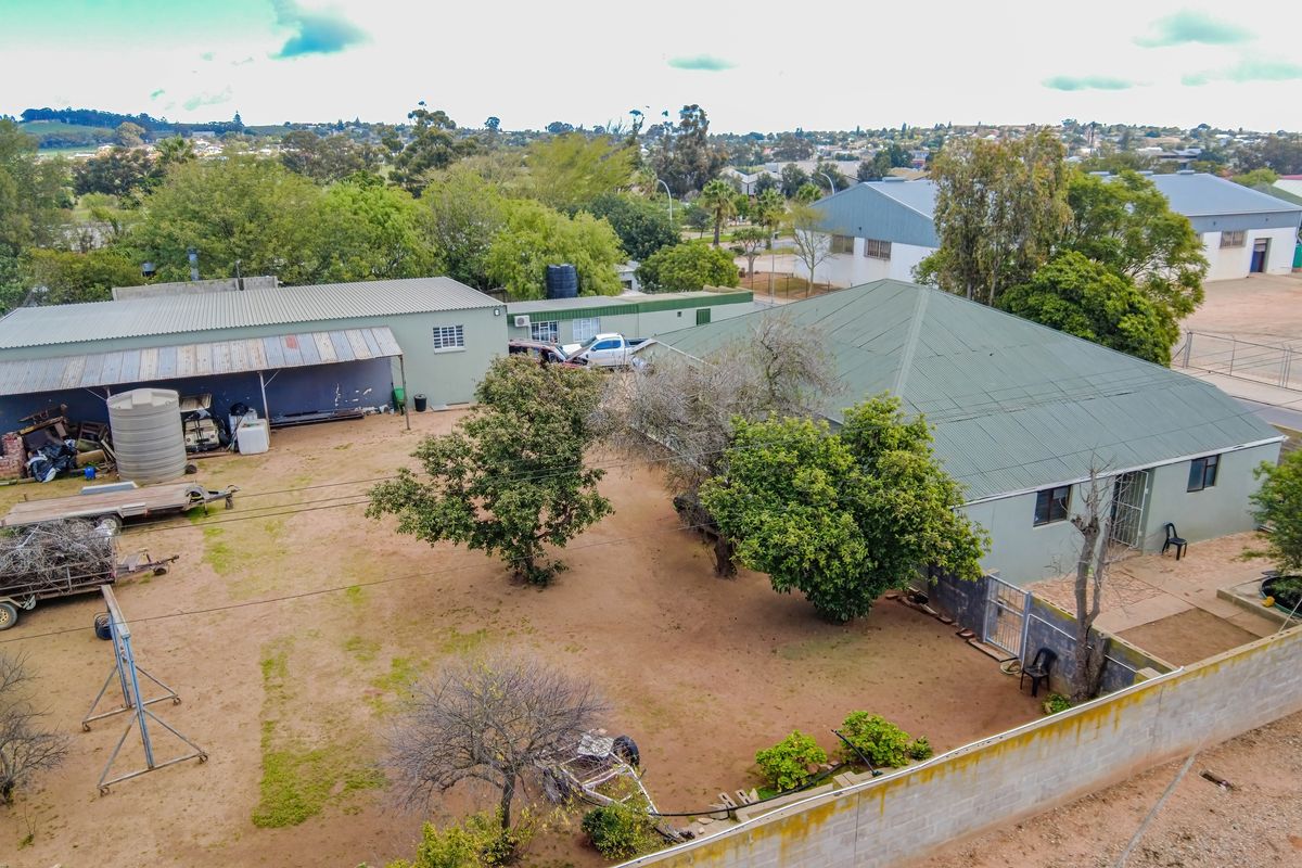Aerial view of the property showing the main dwelling, adjacent outbuildings, large unpaved yard, and surrounding boundary walls.