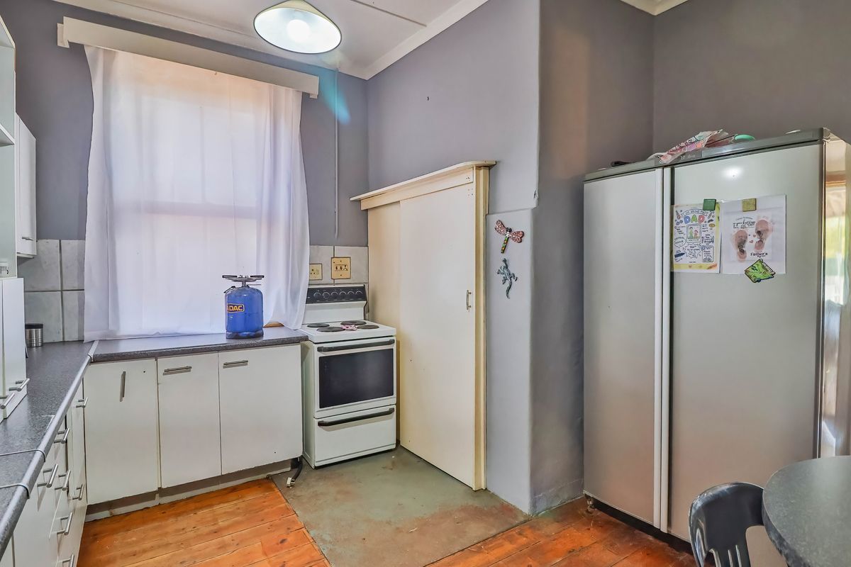 A functional kitchen featuring white cabinetry, laminate countertops, a freestanding stove, and original timber flooring, offering potential for cosmetic updates and modernization.