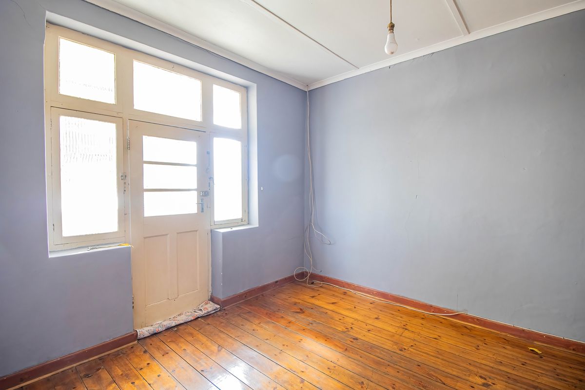 An empty living room featuring original timber flooring, large timber-framed windows, and a matching door with direct access to the exterior.