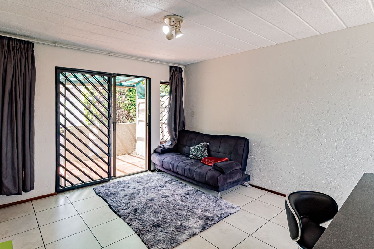 A living room featuring tiled flooring and a sliding glass door with a security gate, providing direct access to an outdoor patio area.