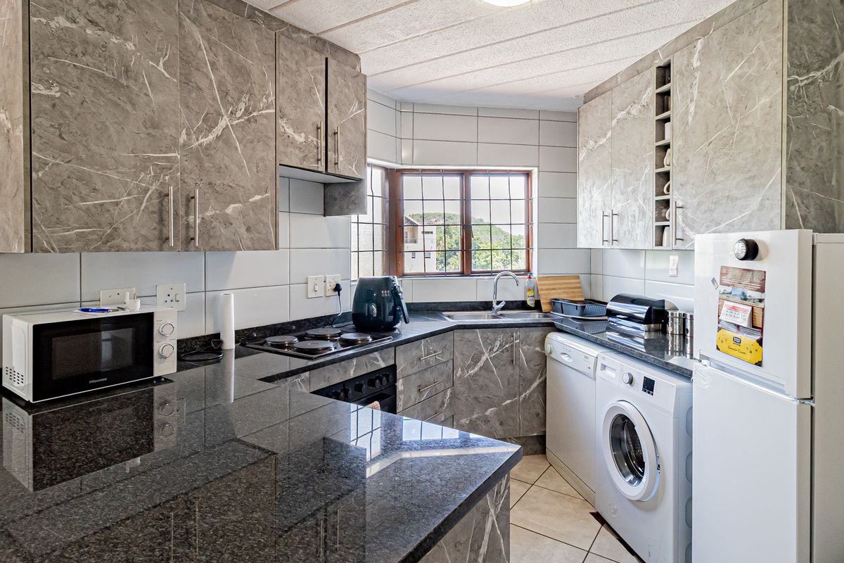 A functional kitchen featuring marble-effect cabinetry, granite countertops, a built-in hob and oven, and tiled finishes with a window view.