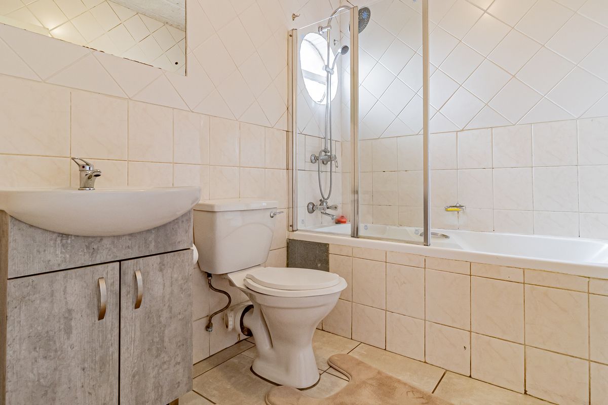 A functional bathroom featuring a vanity cabinet, toilet, and a bathtub with a glass shower screen, finished with neutral wall tiling.