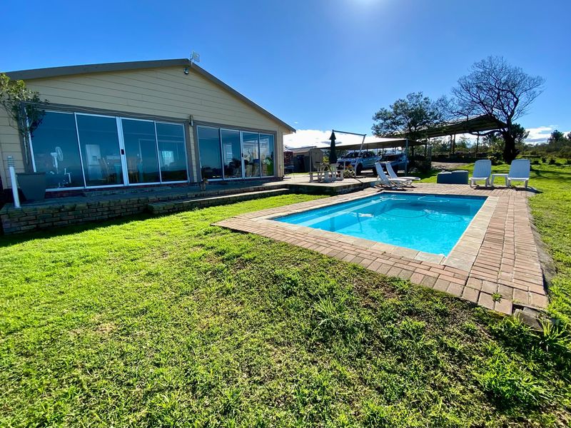 Rear exterior view of the farmhouse featuring a swimming pool with brick coping, a lawn area, and large sliding glass doors leading indoors.