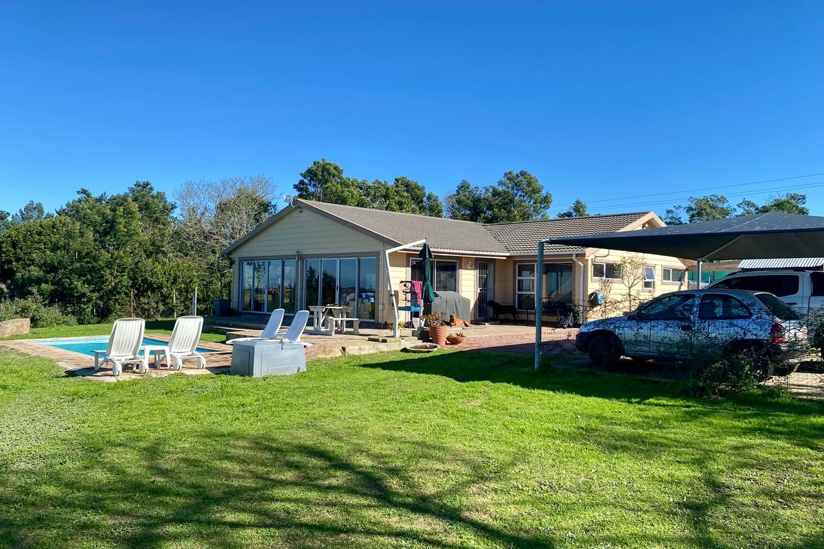 Rear view of the farm property featuring a swimming pool, paved patio area, and a carport structure set against a large lawn.