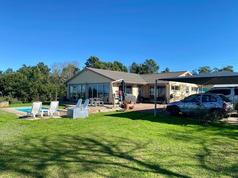 Rear view of the farm property featuring a swimming pool, paved patio area, and a carport structure set against a large lawn.