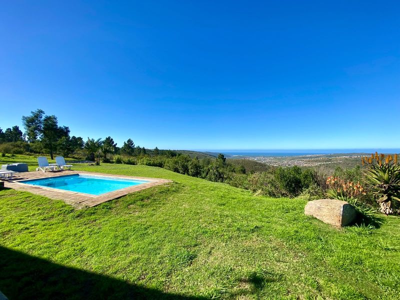 Outdoor swimming pool area set within a spacious garden, featuring expansive panoramic views of the surrounding landscape and distant coastline.