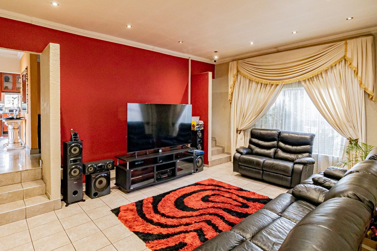 Spacious living room featuring tiled flooring, recessed downlighting, and a bold red accent wall, with an open transition to the adjacent kitchen area.