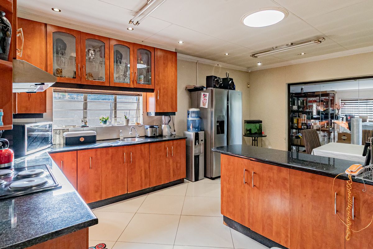 Spacious kitchen featuring warm-toned wooden cabinetry, granite countertops, integrated appliances, and a functional layout with a central island and ample storage space.