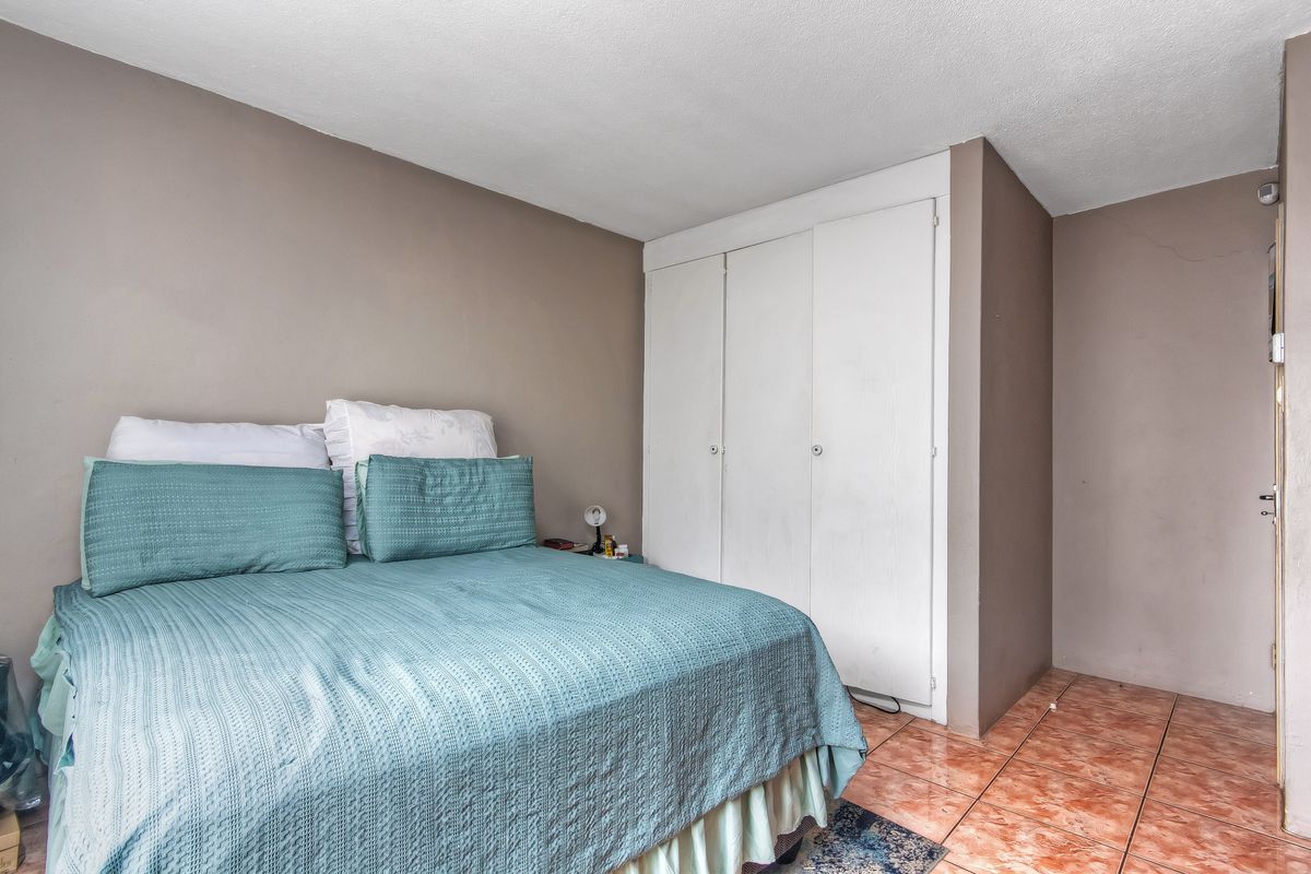 A bedroom featuring built-in wardrobe storage and tiled flooring, requiring cosmetic updates to improve the overall aesthetic and condition of the space.
