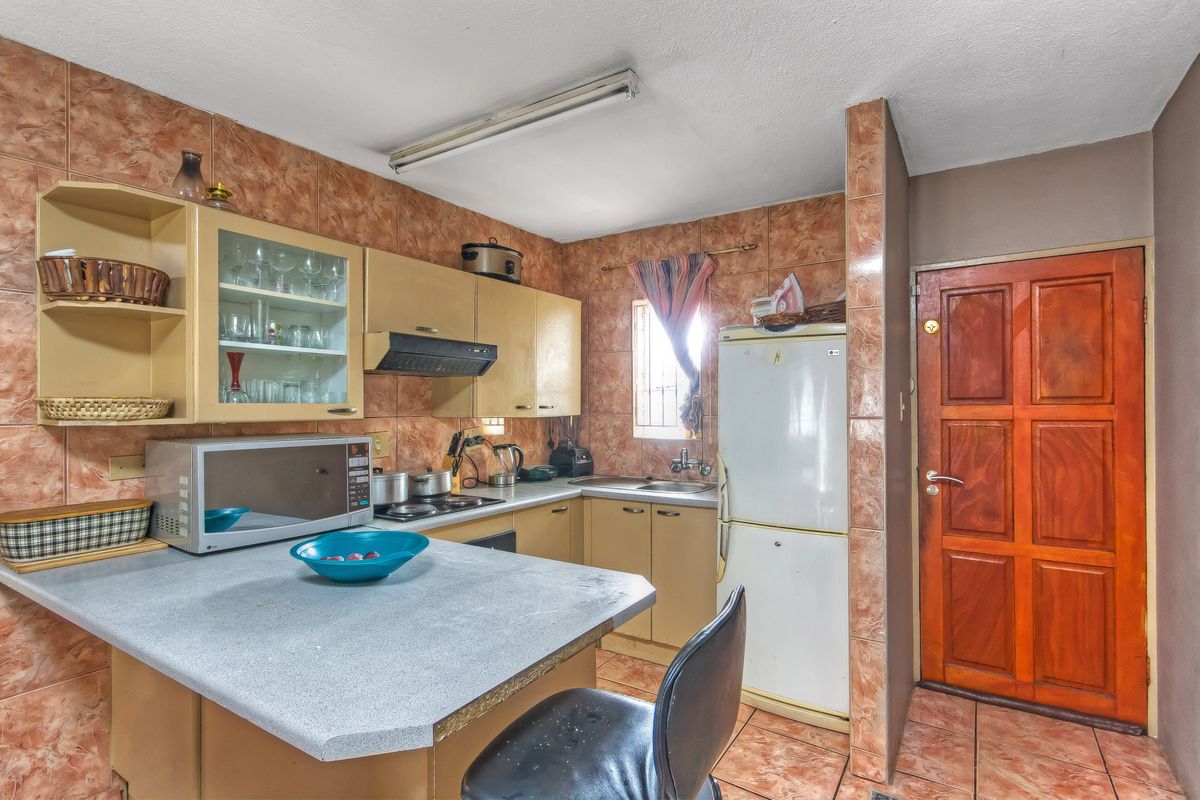 A compact kitchen featuring dated tiled walls, laminate countertops, built-in cabinetry, and a functional layout with a breakfast bar area.