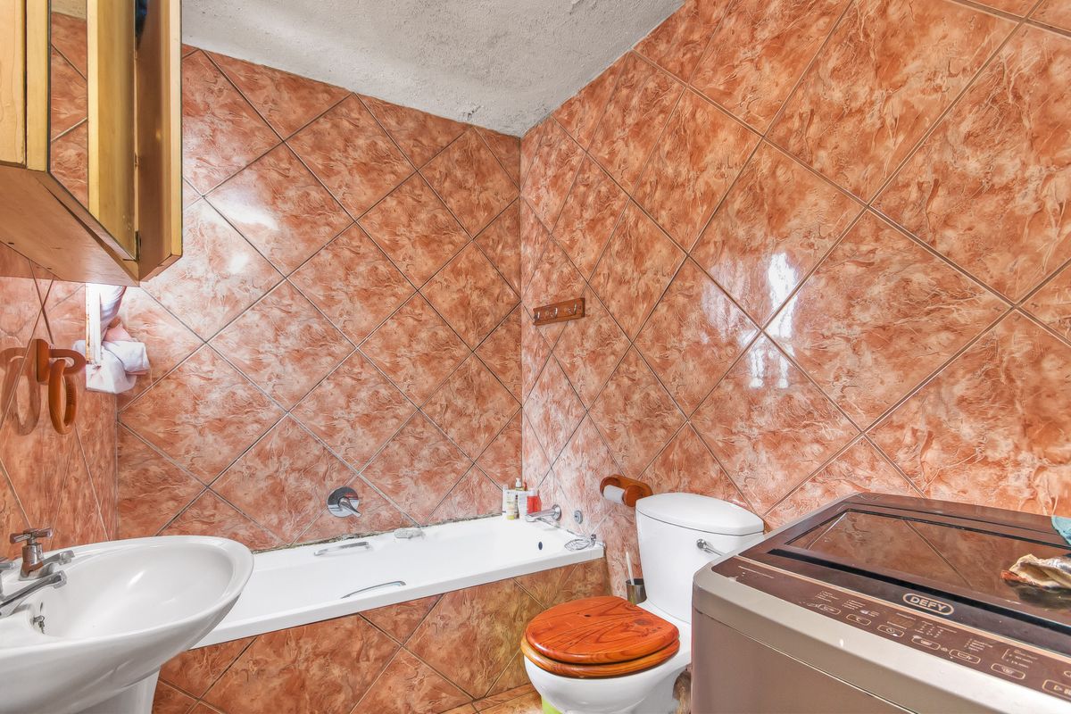 A dated bathroom featuring terracotta-style wall tiles, a pedestal basin, a bathtub, and a toilet, with visible wear on the ceiling and finishes.