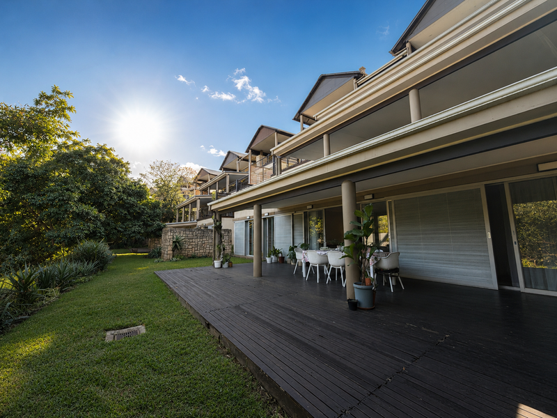 Spacious rear timber deck overlooking a landscaped garden, featuring covered patio areas and large sliding glass doors providing seamless indoor-outdoor flow.