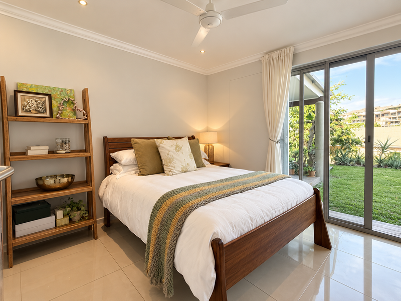 A bright and well-maintained bedroom featuring tiled flooring, a ceiling fan, and large sliding glass doors providing direct access to the garden.
