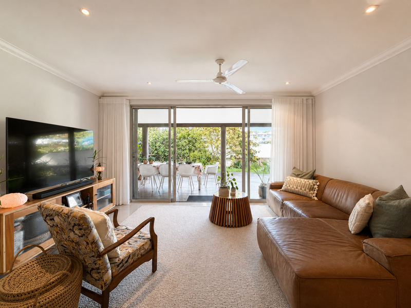 A bright and inviting living room featuring recessed lighting, a ceiling fan, and large sliding glass doors that open onto an outdoor patio area.