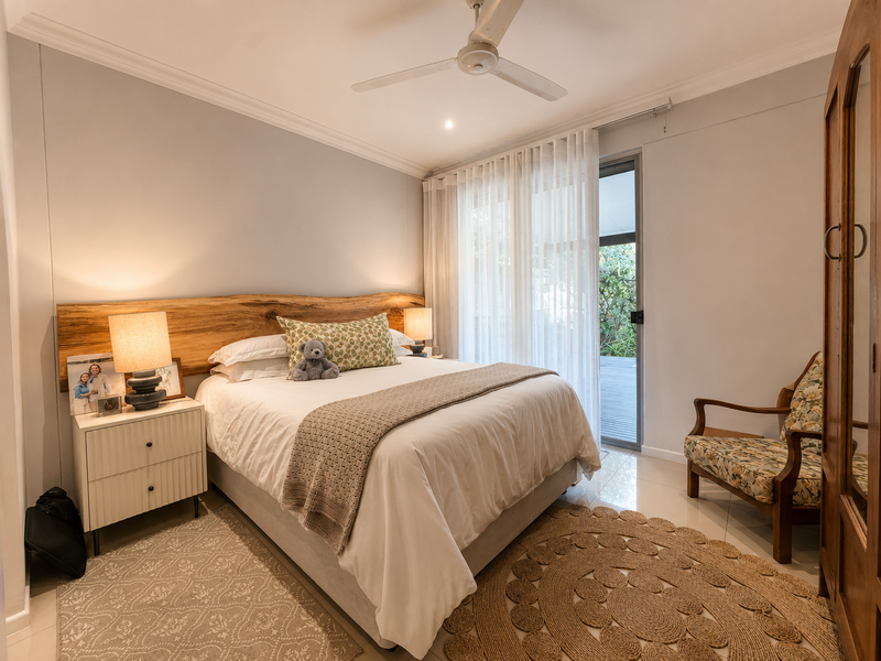 A well-maintained bedroom featuring tiled flooring, a ceiling fan, and direct access to an outdoor area through a sliding glass door.