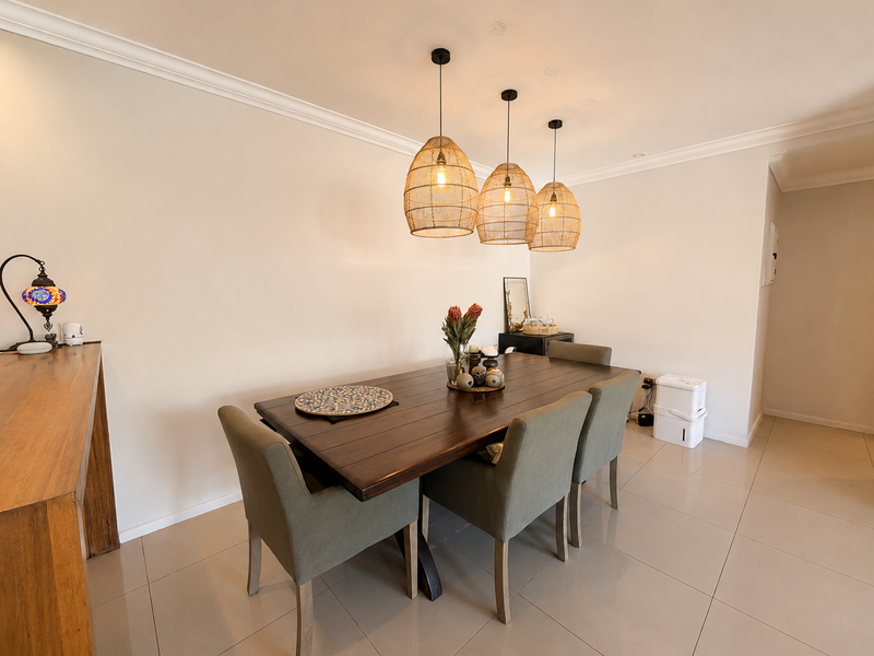 A well-maintained dining area featuring neutral tiled flooring, decorative pendant lighting, and classic cove cornicing, creating a bright and inviting space.