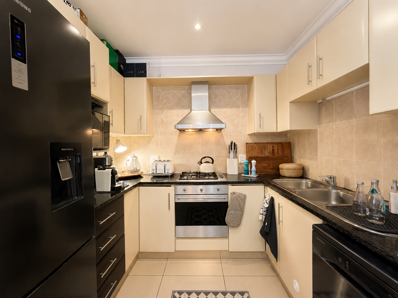 A well-maintained kitchen featuring cream cabinetry, granite countertops, a stainless steel gas hob, oven, extractor fan, and a double bowl sink.