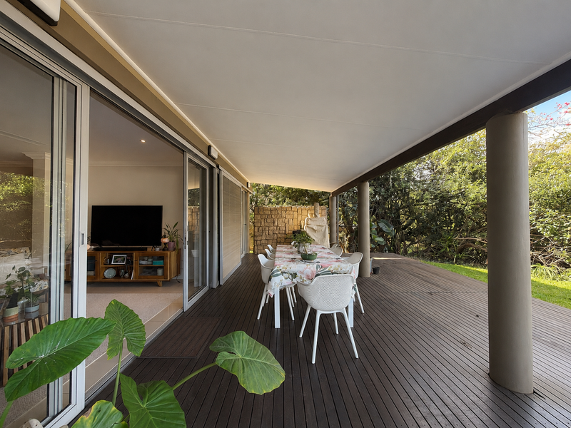 Spacious covered patio featuring timber decking, stone feature wall, and large sliding glass doors providing seamless indoor-outdoor flow to the garden area.