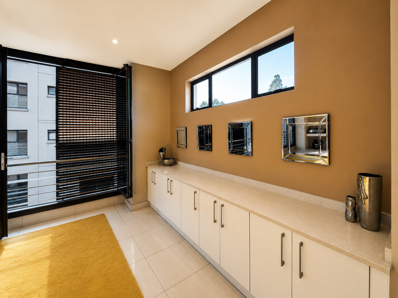 A bright living area featuring extensive built-in cabinetry with stone countertops, large bi-fold doors opening to a balcony, and modern tiled flooring.
