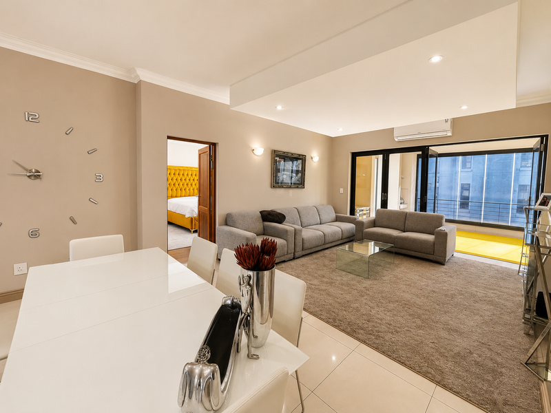 Spacious open-plan living and dining area featuring tiled and carpeted floors, recessed ceiling lighting, and bi-fold doors leading to a balcony.