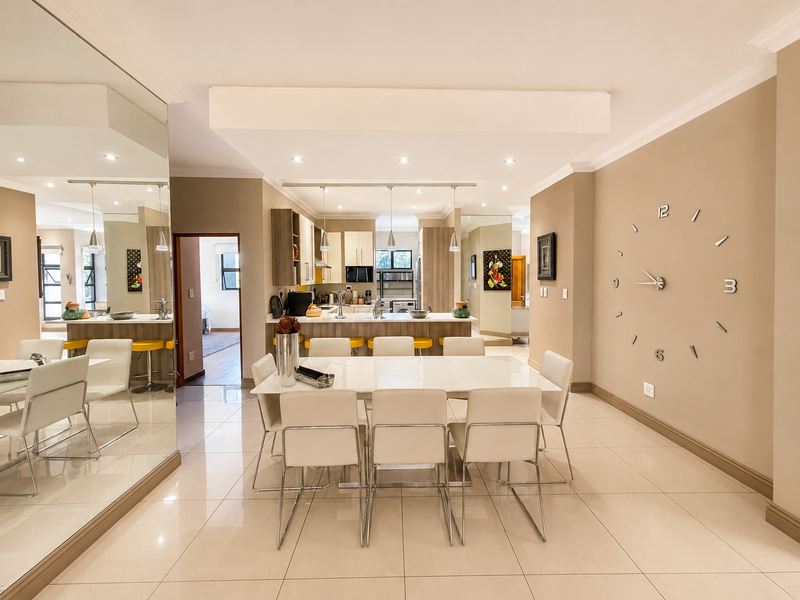 Spacious open-plan dining and kitchen area featuring modern cabinetry, a central island, tiled flooring, and a large feature mirror wall.