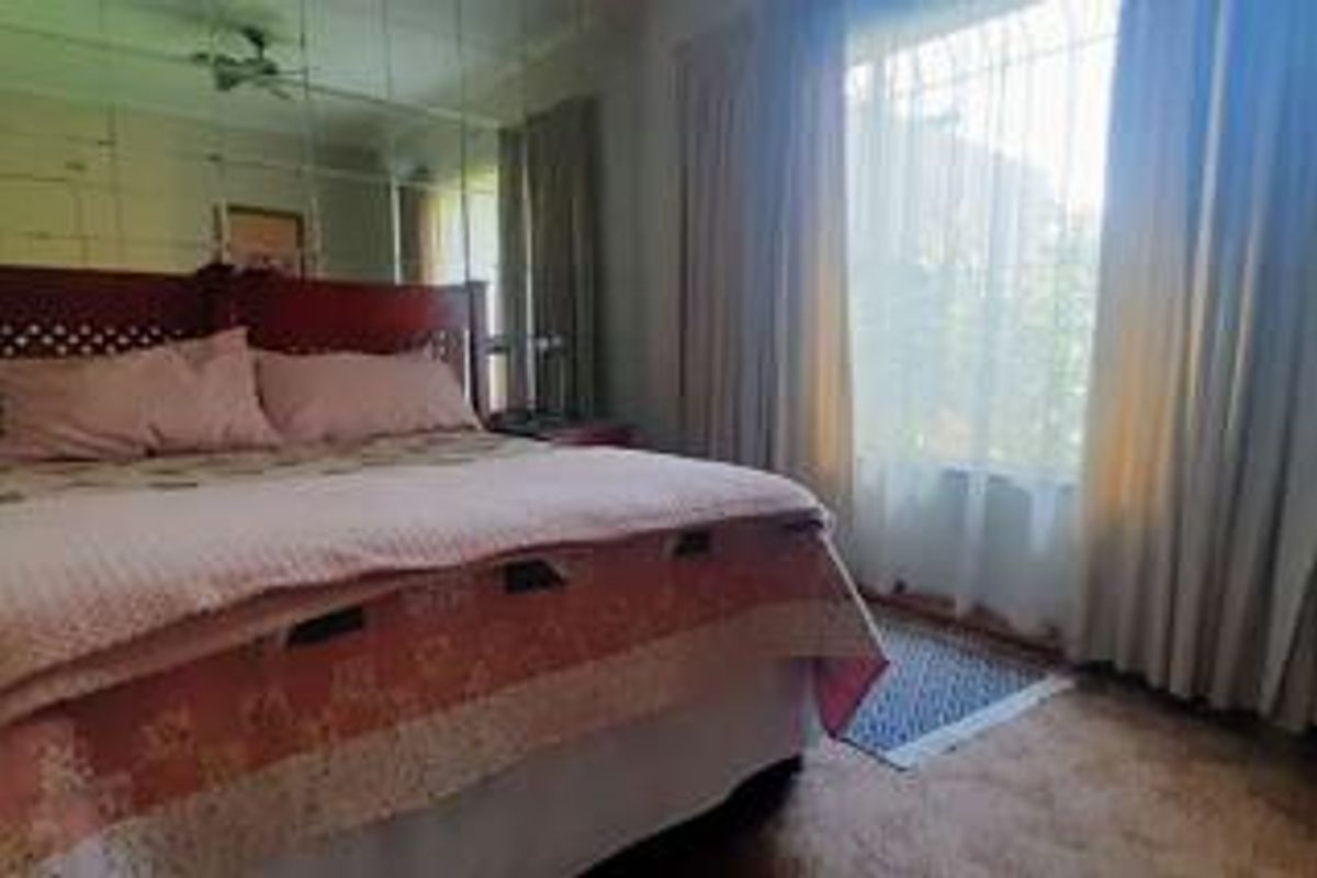 A bedroom featuring a large mirrored wall and a window with security bars, currently finished with dated carpeting and wall treatments.