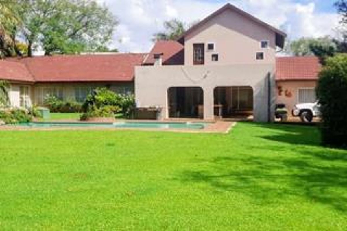 Rear view of the property featuring a spacious lawn, swimming pool, and a covered patio area attached to the main dwelling.