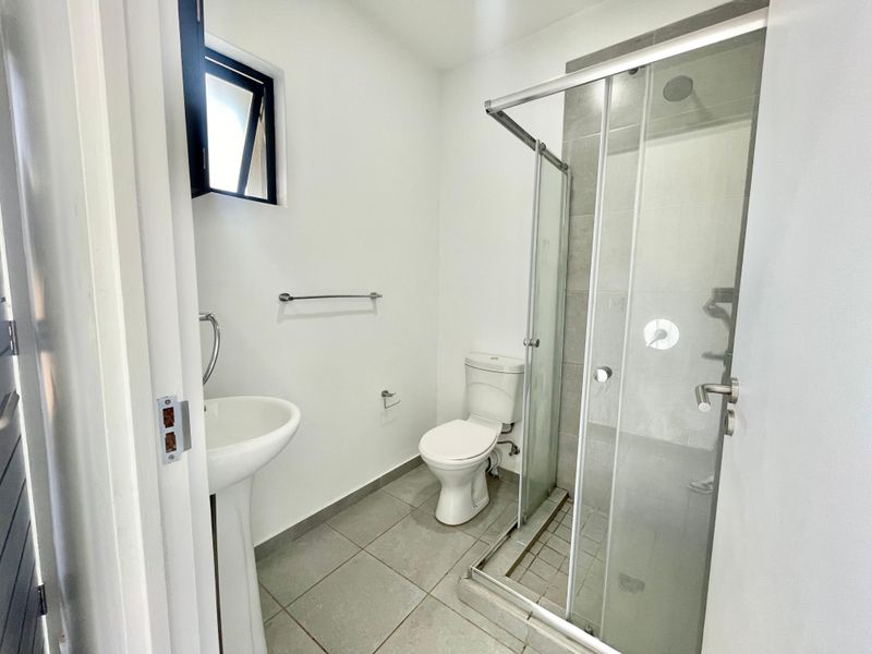 A clean, modern bathroom featuring a pedestal basin, a toilet, and a glass-enclosed shower with neutral floor tiling.