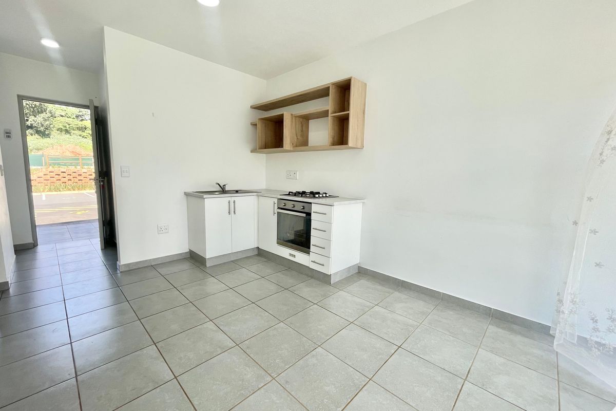 A compact, modern kitchen featuring white cabinetry, built-in oven, gas hob, and open shelving, set against neutral tiled flooring in an open-plan layout.