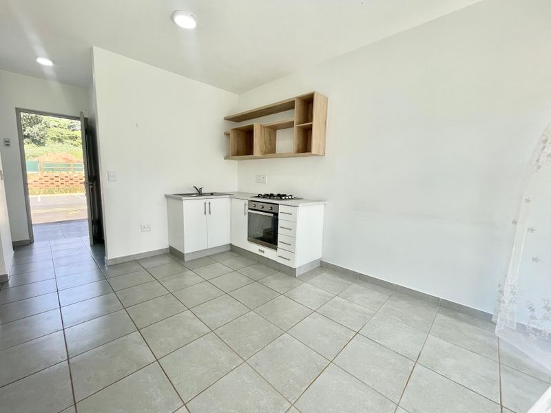 A compact, modern kitchen featuring white cabinetry, built-in oven, gas hob, and open shelving, set against neutral tiled flooring in an open-plan layout.