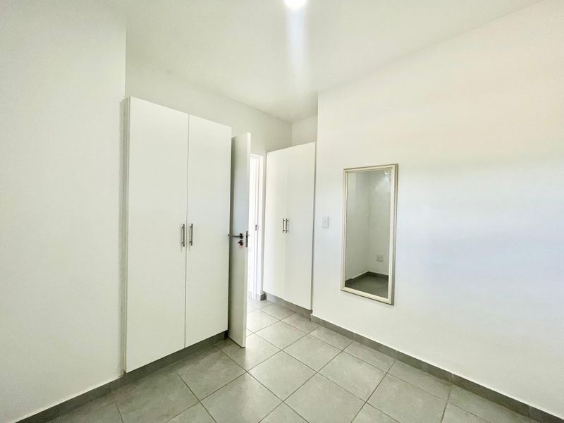 A clean, minimalist hallway featuring neutral tiled flooring and ample built-in cupboard storage, providing a bright and functional transition space.