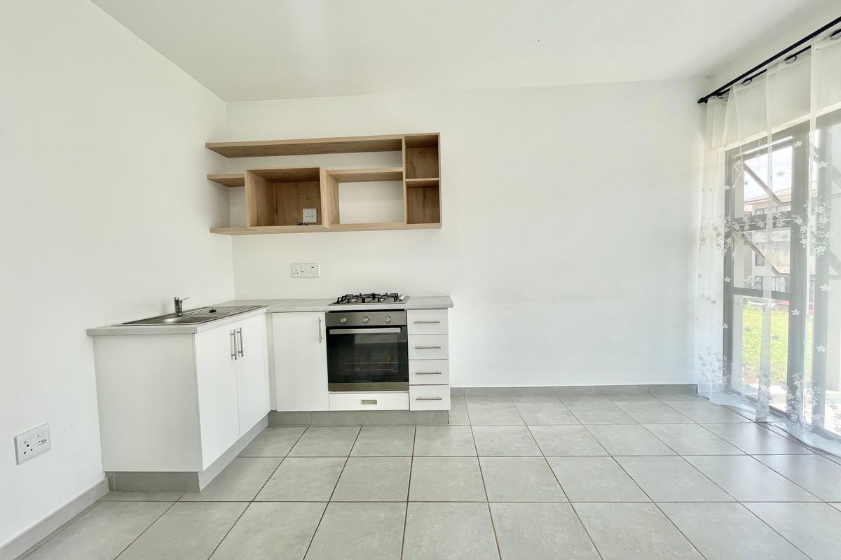 A clean, modern kitchen featuring white cabinetry, built-in oven and gas hob, open shelving, and tiled flooring with direct access to an outdoor area.