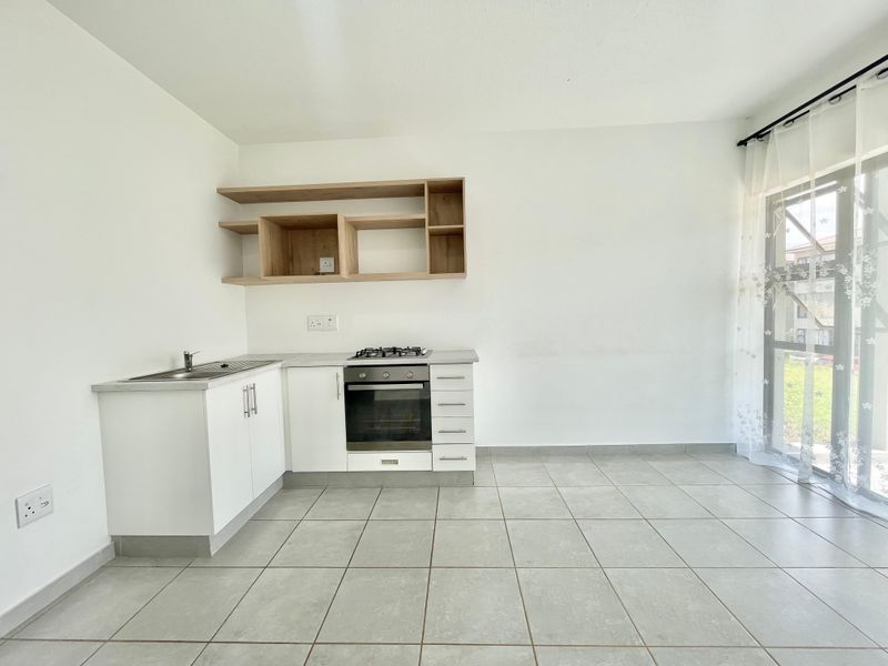 A clean, modern kitchen featuring white cabinetry, built-in oven and gas hob, open shelving, and tiled flooring with direct access to an outdoor area.