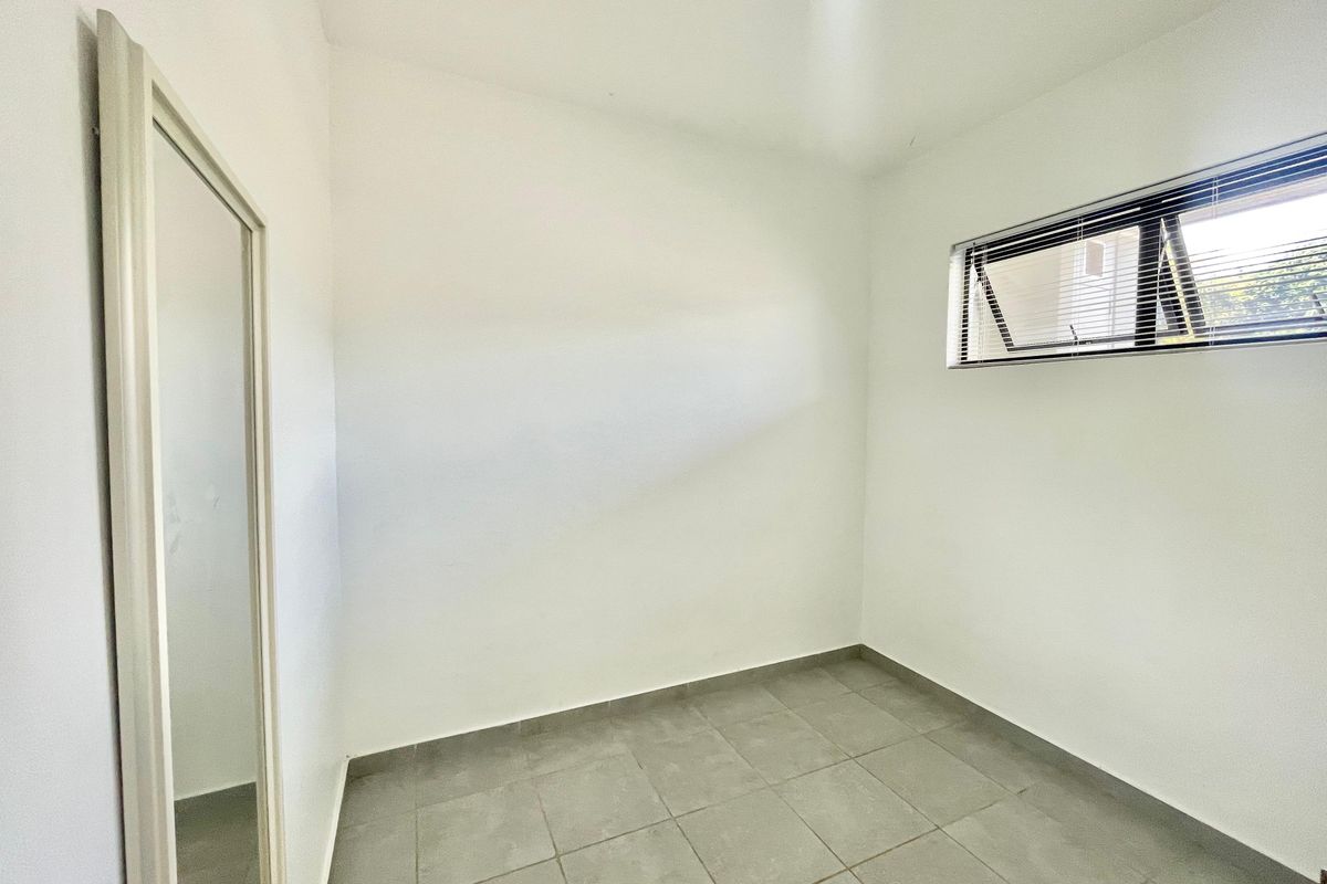 A clean, empty bedroom featuring neutral tiled flooring, white walls, and a top-hung window with fitted venetian blinds.