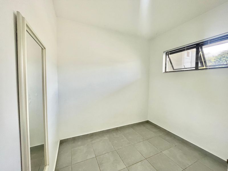 A clean, empty bedroom featuring neutral tiled flooring, white walls, and a top-hung window with fitted venetian blinds.