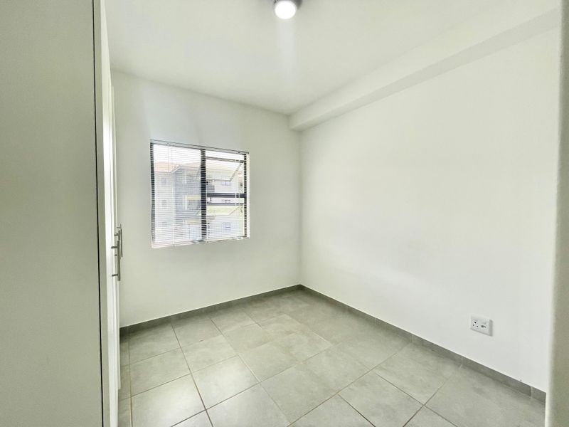 A clean, empty bedroom featuring neutral tiled flooring, a built-in cupboard, and a window fitted with venetian blinds.