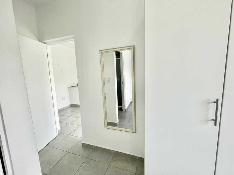 A clean, neutral hallway featuring tiled flooring and a built-in cupboard, providing access to adjacent rooms.