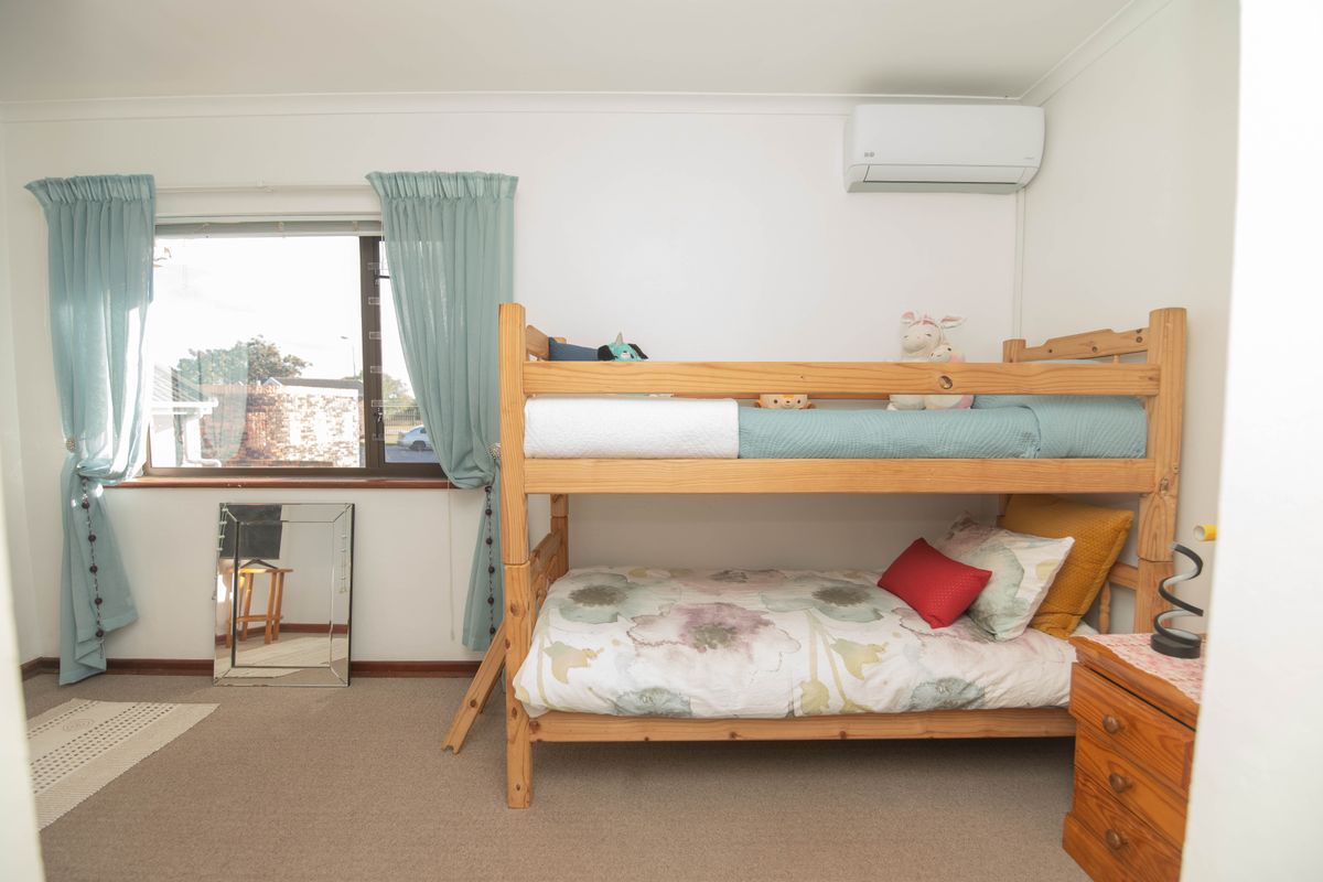 A functional bedroom featuring carpeted flooring, a window with curtains, and a wall-mounted split-system air conditioning unit.