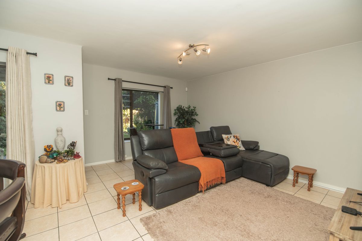 A living room featuring neutral tiled flooring, a sliding glass door providing garden access, and modern track lighting.