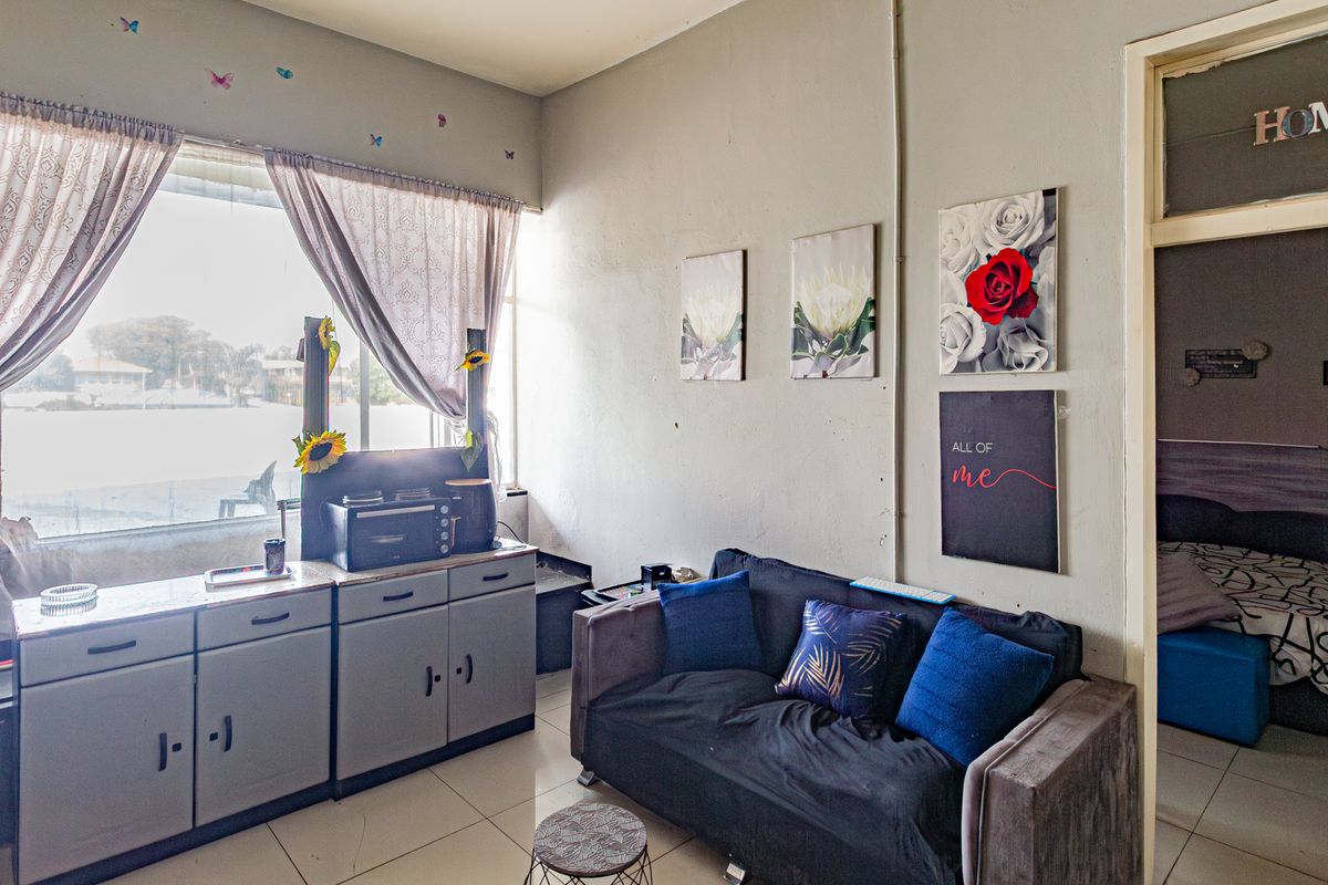 A living area featuring tiled flooring and a large window, showing signs of wear on the walls that would benefit from cosmetic updates.