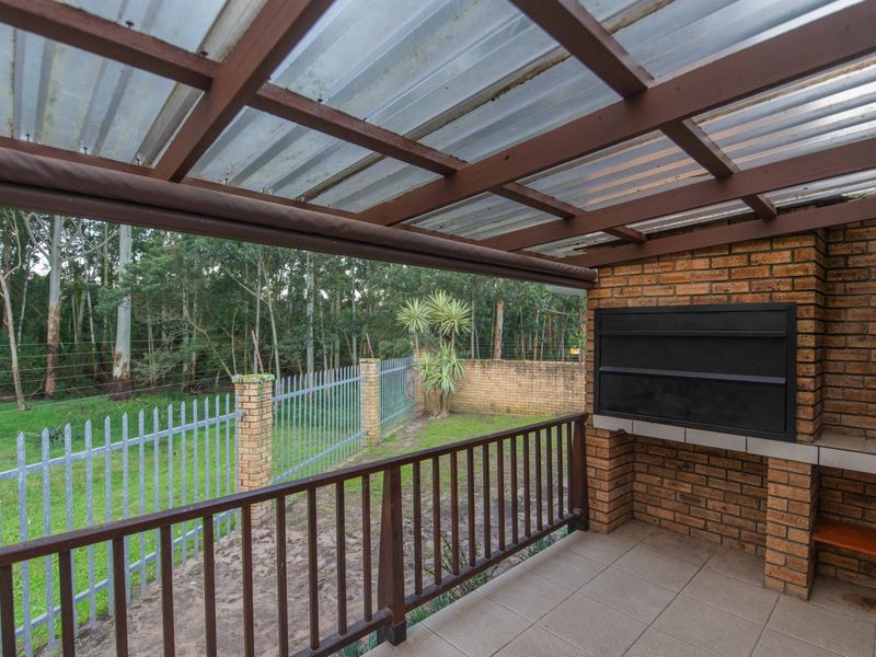 Covered patio featuring a built-in braai, timber pergola structure, and tiled flooring, overlooking a private garden area.