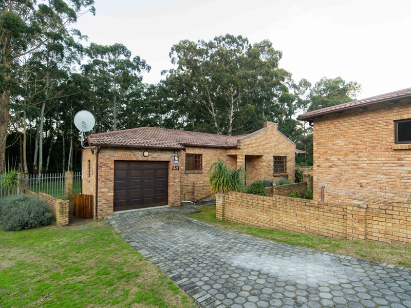 Front view of a face brick townhouse featuring a single garage, paved driveway, and established garden surroundings.