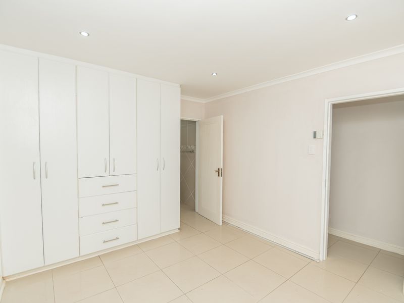A bright, empty bedroom featuring neutral tiled flooring, recessed downlighting, and extensive white built-in cabinetry with integrated drawers.