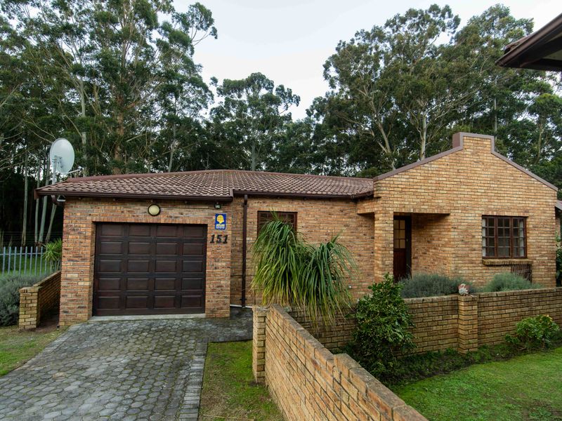 Front view of a face-brick townhouse featuring a single garage, paved driveway, and a low brick boundary wall.