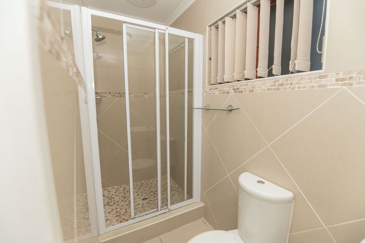 A clean bathroom featuring a shower enclosure with pebble-style flooring, a toilet, and neutral wall tiling with a decorative border.