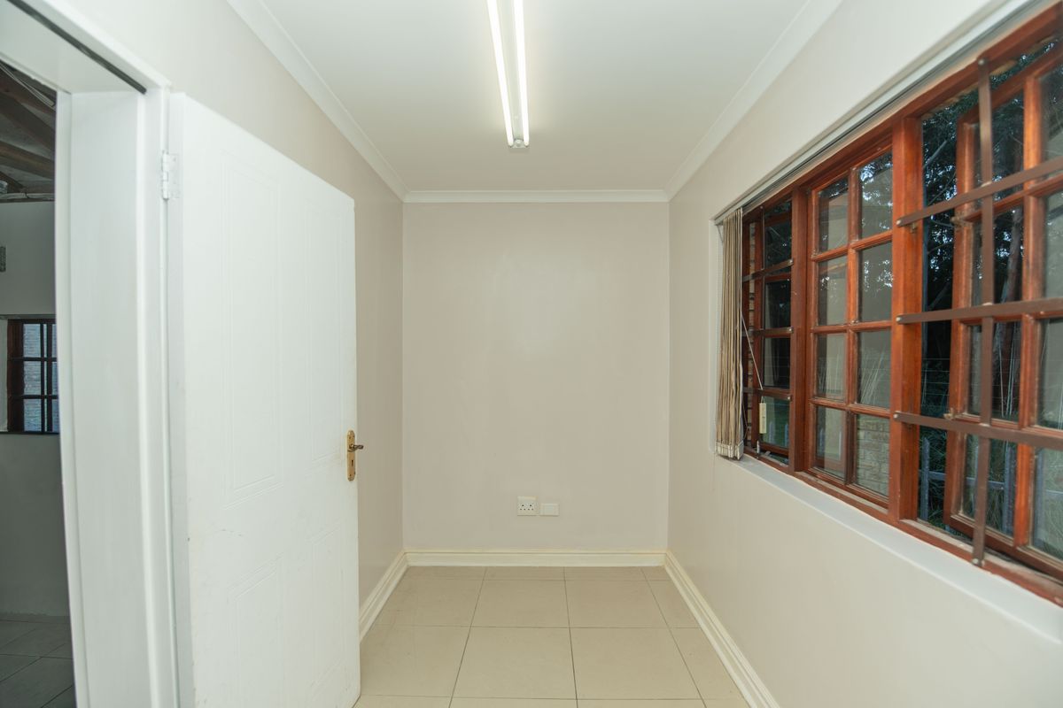 A clean, empty bedroom featuring neutral wall tones, tiled flooring, and large wooden-framed windows with security bars, providing a bright and versatile living space.