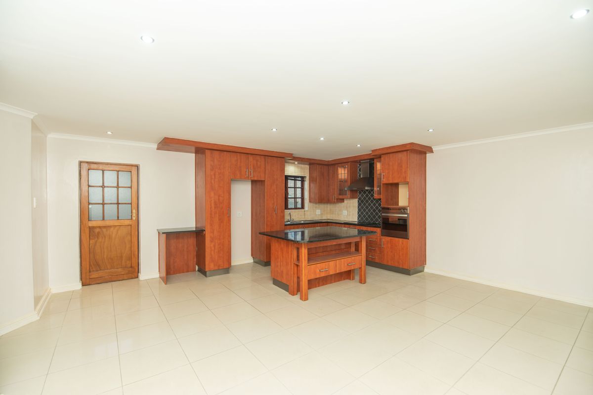 Spacious kitchen featuring warm-toned wooden cabinetry, a central island with granite countertops, built-in oven, and tiled flooring in an open-plan layout.
