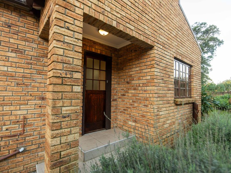 A well-maintained face brick townhouse entrance featuring a covered porch, timber-framed door, and classic window detailing.