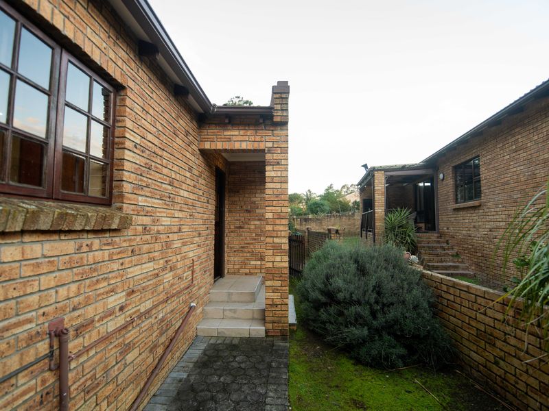 Rear exterior view of a face brick townhouse featuring a paved walkway, entrance steps, and a brick boundary wall.